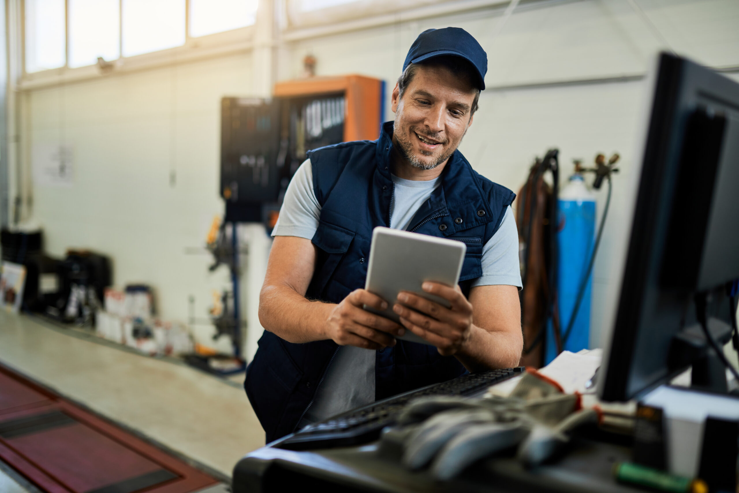 Happy car mechanic using digital tablet while working in auto repair shop.
